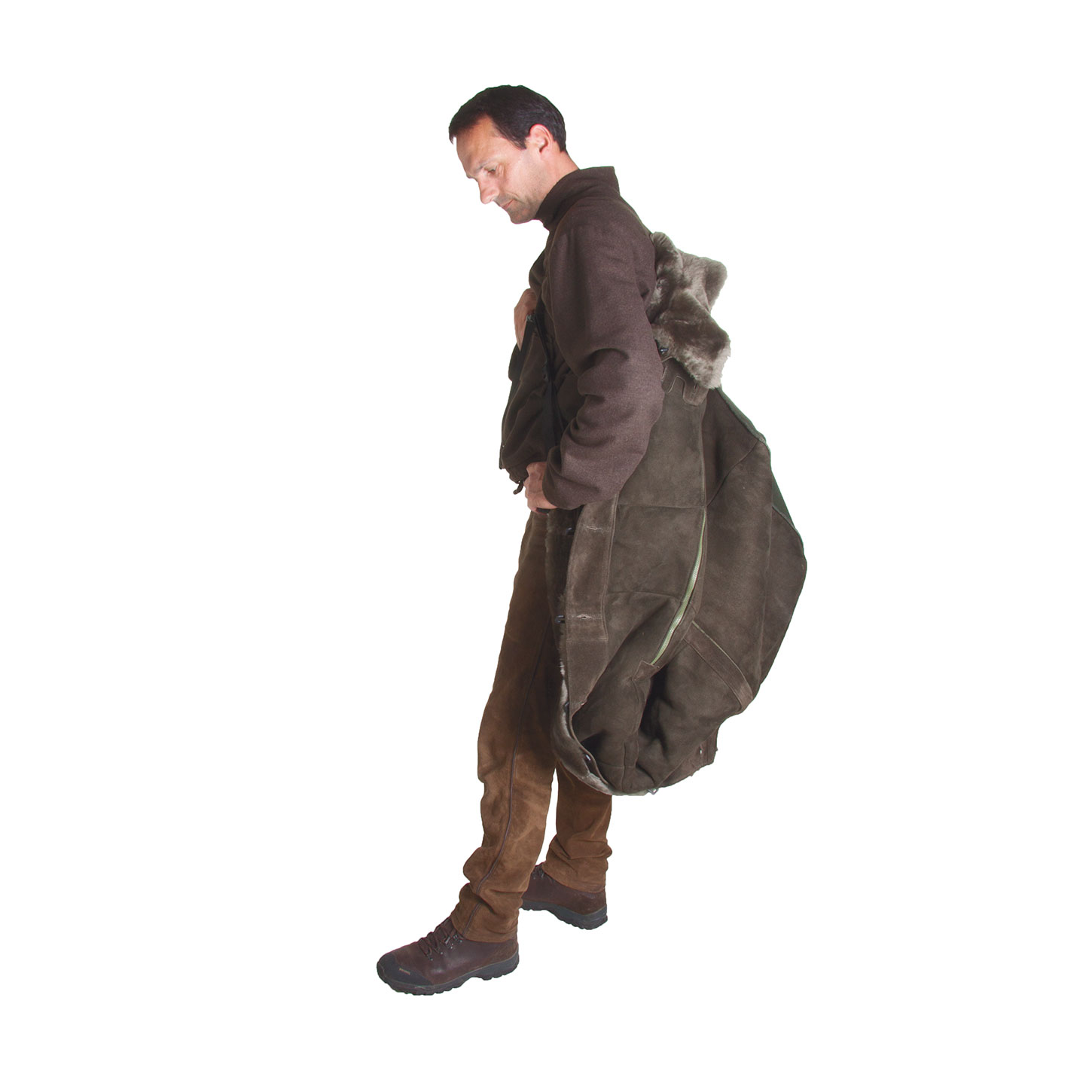 Stehendes Model trägt Überwurf aus echtem Lammfell wie einen Rucksack auf dem Rücken. Der Fußsack ist angezippt und nach hinten hochgeschlagen, reicht bis an die Waden herunter. Seitenansicht.